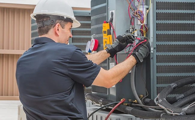Technician testing wiring and electrical components in an outdoor HVAC system